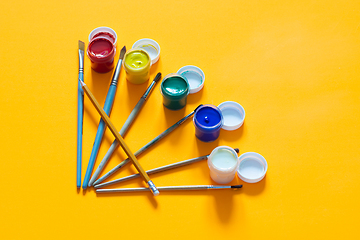 Image showing Brushes and one pencil are laid out on the table, jars of gouache are nearby