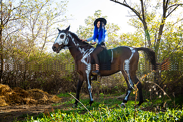 Image showing A girl dressed as a witch rides a horse on which a skeleton is painted in white paint