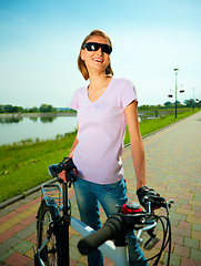 Image showing Young woman is standing behind bicycle