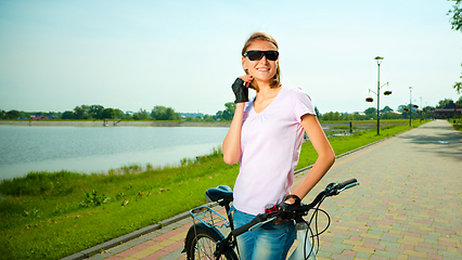 Image showing Young woman is standing behind bicycle