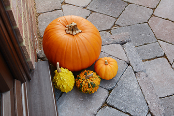 Image showing Pumpkin surrounded by ornamental gourds on a doorstep 