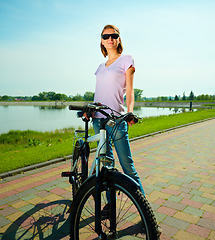 Image showing Young woman is standing behind bicycle