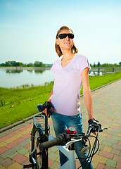 Image showing Young woman is standing behind bicycle