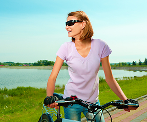 Image showing Young woman is standing behind bicycle