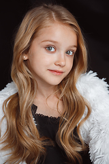 Image showing Little smiling girl posing in white outfit on black studio background