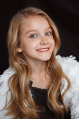 Image showing Little smiling girl posing in white outfit on black studio background