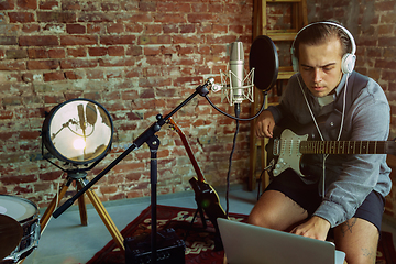 Image showing Young man recording music, playing guitar and singing at home