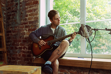 Image showing Young man recording music, playing guitar and singing at home