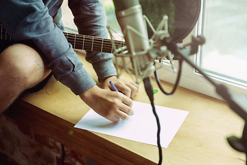 Image showing Young man recording music, playing guitar and singing at home