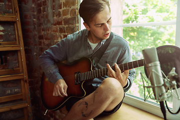 Image showing Young man recording music, playing guitar and singing at home