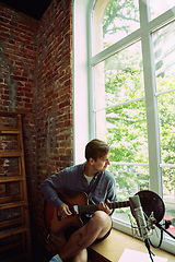 Image showing Young man recording music, playing guitar and singing at home