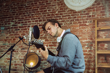 Image showing Young man recording music, playing guitar and singing at home