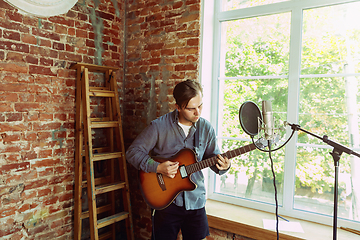 Image showing Young man recording music, playing guitar and singing at home