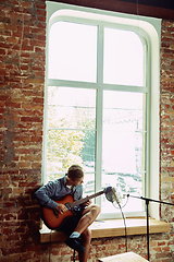 Image showing Young man recording music, playing guitar and singing at home