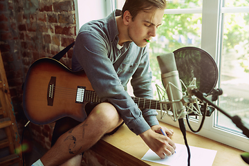 Image showing Young man recording music, playing guitar and singing at home