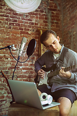 Image showing Young man recording music, playing guitar and singing at home