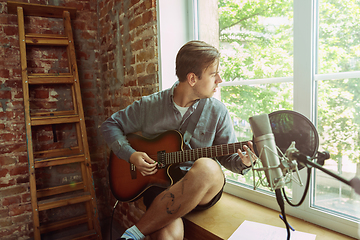 Image showing Young man recording music, playing guitar and singing at home