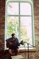 Image showing Young man recording music, playing guitar and singing at home