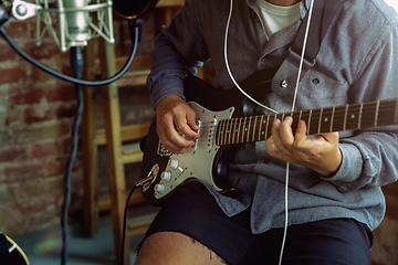 Image showing Young man recording music, playing guitar and singing at home