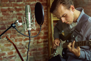 Image showing Young man recording music, playing guitar and singing at home