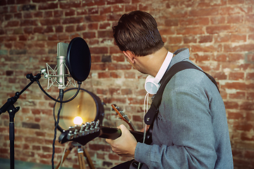 Image showing Young man recording music, playing guitar and singing at home