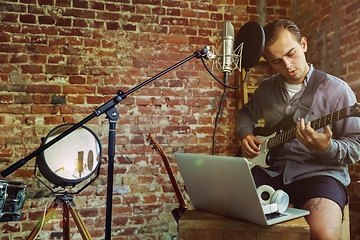 Image showing Young man recording music, playing guitar and singing at home