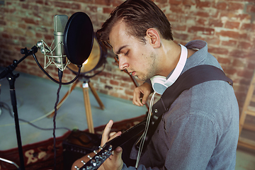 Image showing Young man recording music, playing guitar and singing at home