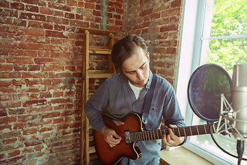 Image showing Young man recording music, playing guitar and singing at home