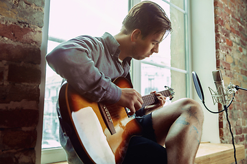 Image showing Young man recording music, playing guitar and singing at home