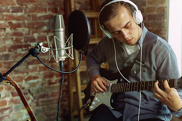 Image showing Young man recording music, playing guitar and singing at home