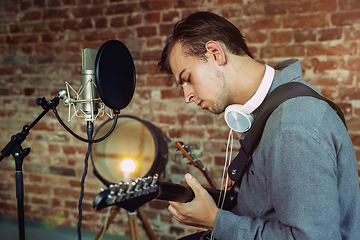 Image showing Young man recording music, playing guitar and singing at home