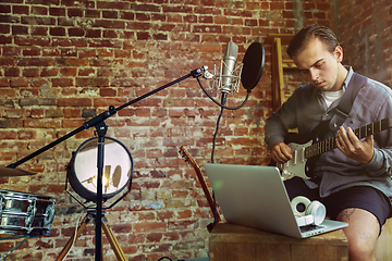 Image showing Young man recording music, playing guitar and singing at home