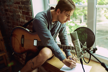 Image showing Young man recording music, playing guitar and singing at home