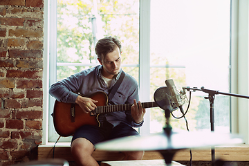 Image showing Young man recording music, playing guitar and singing at home