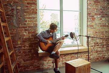 Image showing Young man recording music, playing guitar and singing at home