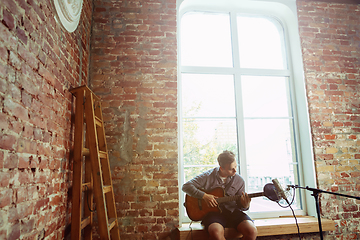 Image showing Young man recording music, playing guitar and singing at home