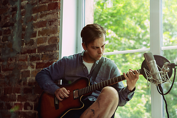 Image showing Young man recording music, playing guitar and singing at home