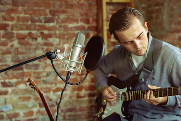 Image showing Young man recording music, playing guitar and singing at home