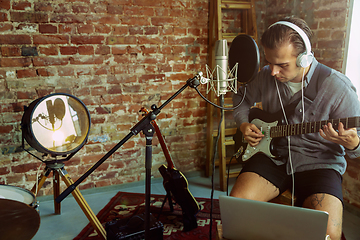 Image showing Young man recording music, playing guitar and singing at home