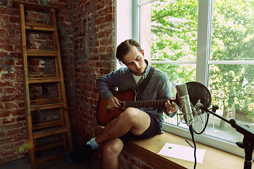 Image showing Young man recording music, playing guitar and singing at home