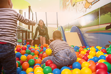 Image showing young mom playing with kids in pool with colorful balls