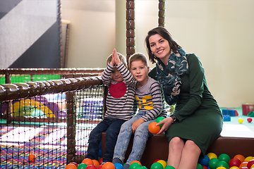 Image showing young mom playing with kids in pool with colorful balls