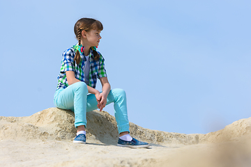 Image showing A teenage girl crouched on the top of a mountain and resting examines the surroundings