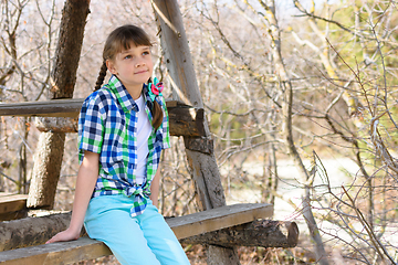 Image showing A girl sits on a wooden bench in the forest on a warm autumn day and looks into the distance