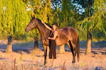 Image showing A girl hugs a horse against a background of trees, the rays of the setting sun fall on them