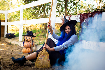 Image showing A girl dressed as a witch sits by the fence, thick white smoke creeps out from behind the fence