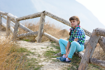 Image showing A girl sits on a fence made of a wooden blockhouse against the background of a landscape