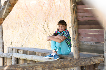 Image showing A ten-year-old girl sits in a wooden gazebo and looks cheerfully into the frame