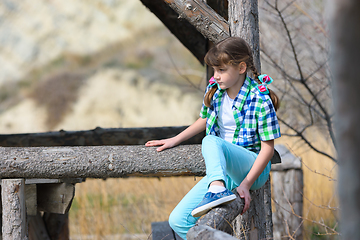 Image showing A girl tries to sit on a fence made of a thick wooden frame