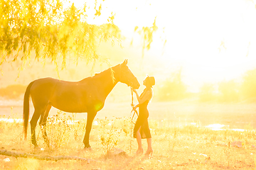 Image showing A girl stands in front of a horse, they are bathed in warm sunbeams at sunset